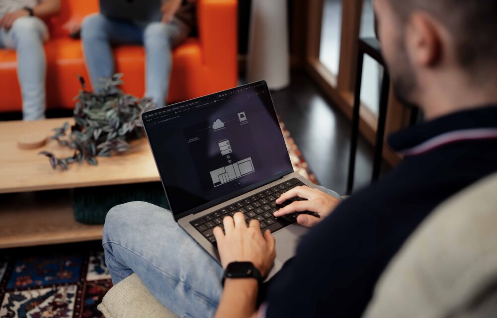 Beeld van achteren, met een medewerker die aan het typen is op een laptop, gezien over zijn schouder