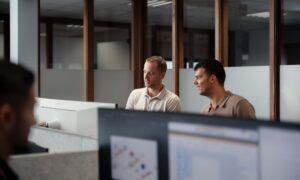 Twee collega's staan naast elkaar achter een bureau en kijken samen naar de computer