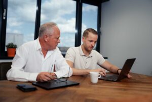 Close-up van twee collega's die in een meeting ruimte zitten, met elkaar in overleg zijn en samen naar het scherm van een collega kijken